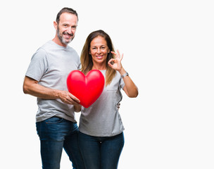 Fototapeta na wymiar Middle age hispanic casual couple in love holding red heart over isolated background doing ok sign with fingers, excellent symbol