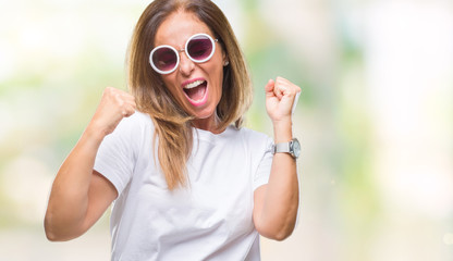 Middle age hispanic woman wearing fashion sunglasses over isolated background very happy and excited doing winner gesture with arms raised, smiling and screaming for success. Celebration concept.