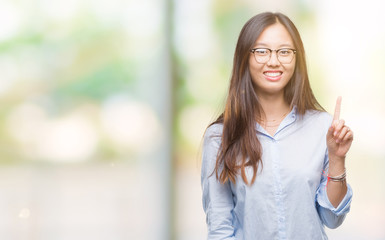 Young asian business woman wearing glasses over isolated background showing and pointing up with finger number one while smiling confident and happy.