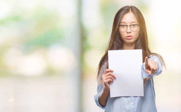 Young Asian Woman Holding Blank Paper Over Isolated Background Pointing With Finger To The Camera And To You, Hand Sign, Positive And Confident Gesture From The Front