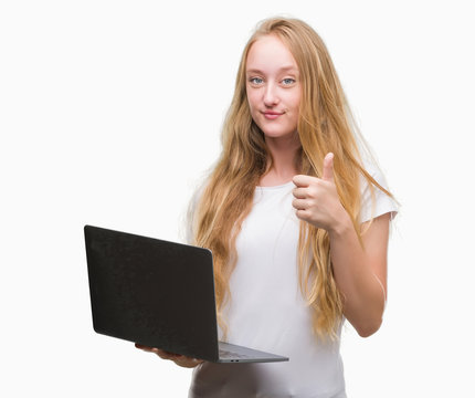 Blonde teenager woman using computer laptop happy with big smile doing ok sign, thumb up with fingers, excellent sign