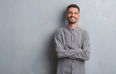 Obraz premium Young adult man standing over grey grunge wall happy face smiling with crossed arms looking at the camera. Positive person.