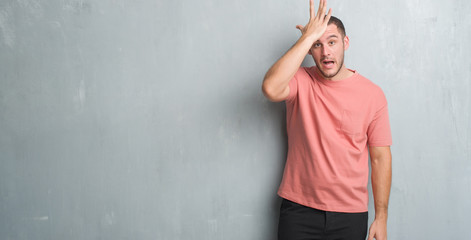 Young caucasian man over grey grunge wall surprised with hand on head for mistake, remember error....
