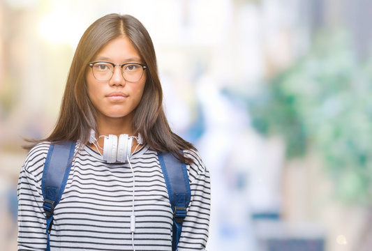 Young Asian Student Woman Wearing Headphones And Backpack Over Isolated Background With Serious Expression On Face. Simple And Natural Looking At The Camera.
