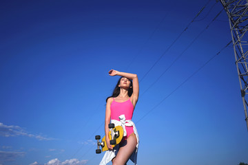 Beautiful sporty girl in pink bikini swimwear holds her yellow longboard with bright blue sky at the background