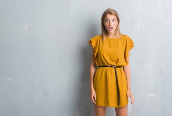 Fototapeta premium Beautiful young woman standing over grunge grey wall wearing a dress afraid and shocked with surprise expression, fear and excited face.