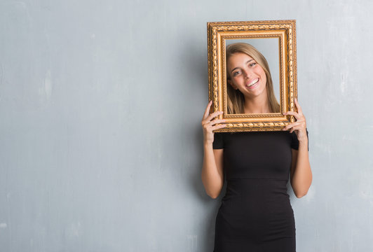 Beautiful young woman over grunge grey wall holding vintage frame with a happy face standing and smiling with a confident smile showing teeth