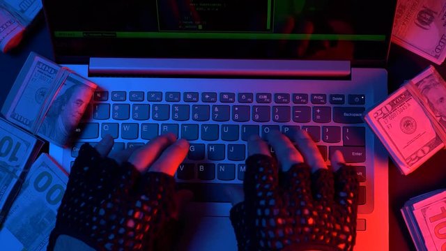 Hacker hacking from his computer with a lot of cash money around his laptop. Randsome criminal concept