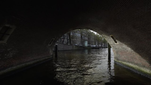 Point of view shot of boat moving under the arch bridge in canal, Amsterdam, Netherlands