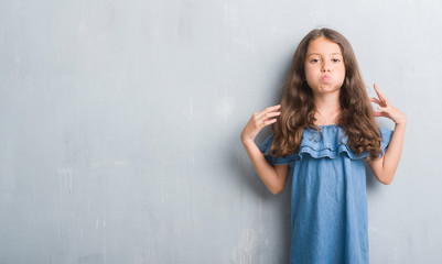 Young hispanic kid over grunge grey wall puffing cheeks with funny face. Mouth inflated with air, crazy expression.