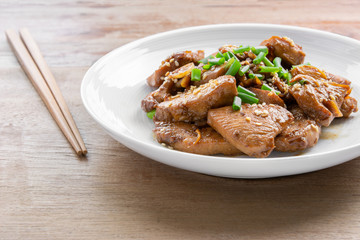close up of stir fried chicken with black soy sauce in a ceramic dish on wooden table. asian homemade style food concept.