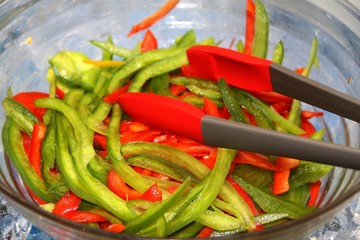 Glass bowl with green and red pepper slices, with red and silver tongs