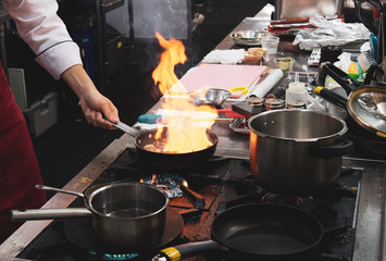 Chef cooking with flame in a frying pan on a kitchen stove