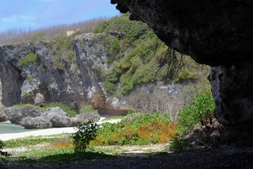 Sharp cliffs and cave-like formations covered with vegetation border a hidden beach in a tropical island  