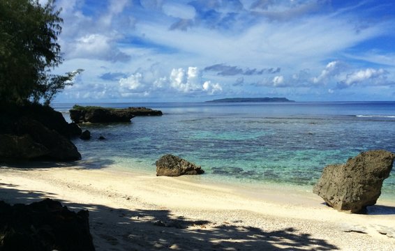 Scenic white sand beach with clear blue skies and waters and rocks  Seen in the distance isthe Goat Island of Tinian, Northern Mariana Islands