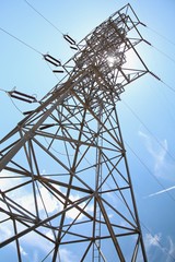 A high voltage power line  with the streak of the sun peeking through on a bright sunny day