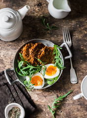Healthy breakfast - sweet potato fritters, boiled egg, arugula salad on wooden background, top view