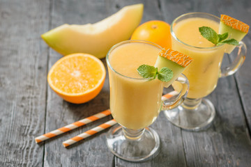 Obraz na płótnie Canvas Melon smoothie, melon, mint, orange and cocktail straws on a dark wooden table.