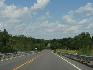 Scenic straight paved road with green vegetation on both sides,  with a background of clear blue and white skies 