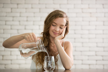 Young woman pouring water from jug into glass in the room