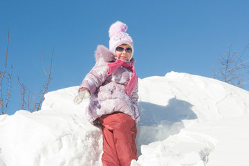 Cheerful girl in dark glasses on the background of a large snowdrift