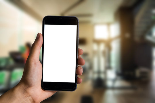 Hand holding white mobile phone with blank white screen  at the corner of the gym.