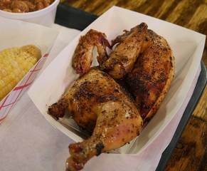 Half of a roasted chicken placed in a paper box, served with beans and corn on the cob