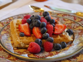 Breakfast of waffles topped with strawberry slices and fresh blueberries
