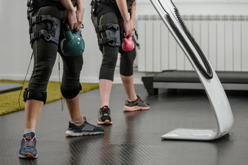 Closeup of two women in EMS suits doing exercises with kettlebell
