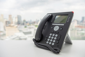 Black IP Phone on the white table with city scape background