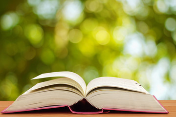 Open book on table in front of green bokeh background