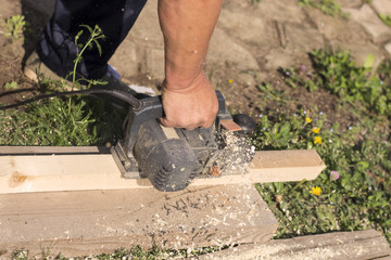 The carpenter works with an electric planer on a wooden Board on the street