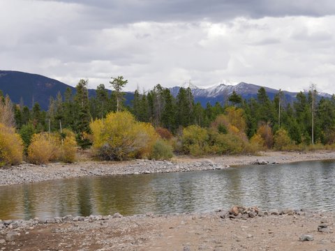 Close up of colorful trees in autumn with water flowing at Dillon Lake in Summit County, Colorado, with the snow-capped mountain peaks in the background.