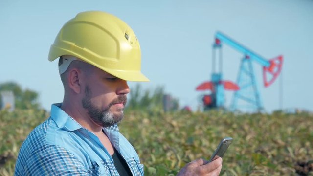 Engineer oilman works with a mobile phone. Oil drill, field pump jack. Oil field, the oil workers are working. The Concept of Oil and Fuel Production.
