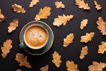 Autumn composition. Cup of coffee and dry leaves on black background. Top view. Flat lay.