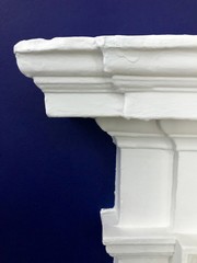 Architectural feature, classically designed mantel painted white against a dark blue background.  