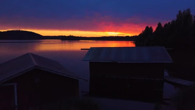 Drone shot of lake with reflection of sky during sunset, huts in foreground, Nurmes, Finland