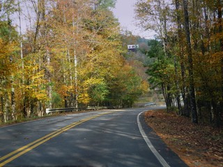 Naklejka premium Winding paved road with colorful leaves from the trees and a log cabin in the background on a beautiful autumn day