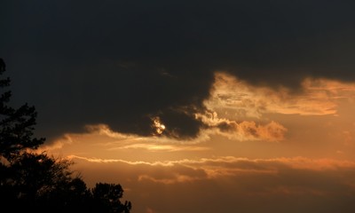 The setting sun partially hidden by dark clouds in the skies 