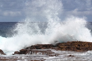 Close up of a giant splash of waves breaking against a coral platform at the beach of a tropical island 