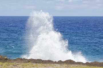 Mesmerizing splashing waves crash against the rocky shoreline of a coast in the tropical area