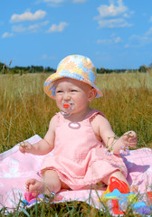 Little girl in a hat sitting on green field
