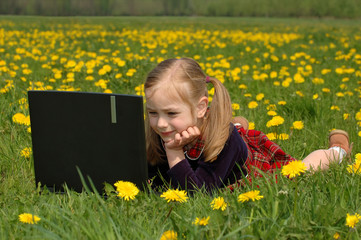 Little girl in a dress with laptop on green meadow