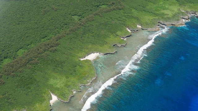 Fototapeta Aerial coastal view of pocket beaches and hidden pools of Tinian, Northern Mariana islands, seen from an airplane window