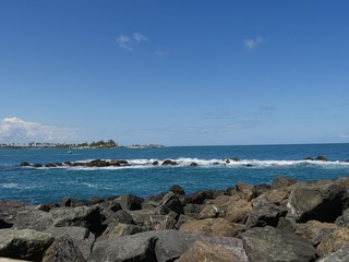 Fototapeta na wymiar Boulders of stones piled right next to the blue waters at the walkway of Fort El Morro in Old San Juan, Puerto Rico. 