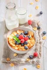 Fresh cornflakes with berry fruits and milk on rustic table