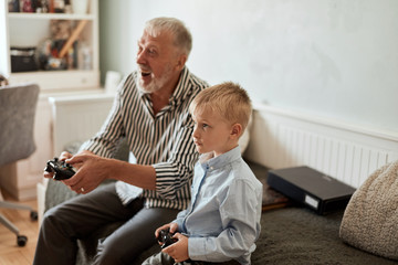 Cute little boy with grandfather sitting on sofa and playing video game with game pad © alfa27