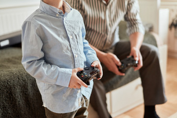 grandfather and grandson playing video game with joysticks in bed room while sitting on couch © alfa27