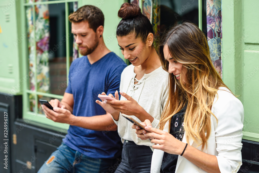 Wall mural group of three people looking down at smart phone smiling