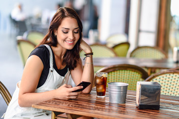 Smiling woman with blue eyes sitting on urban cafe using smart phone